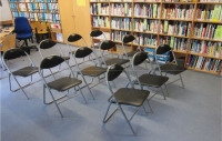 Mehrere Reihen von Stühlen hintereinander gestellt vor Bücherregalen