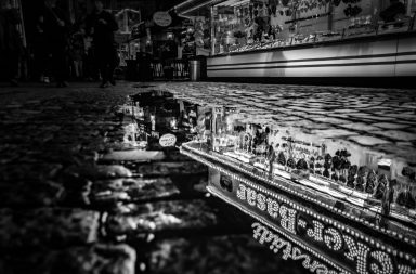 Ein Marktstand spiegelt sich in einer Pfütze auf einem Weg (Schwarz-weiss Bild)