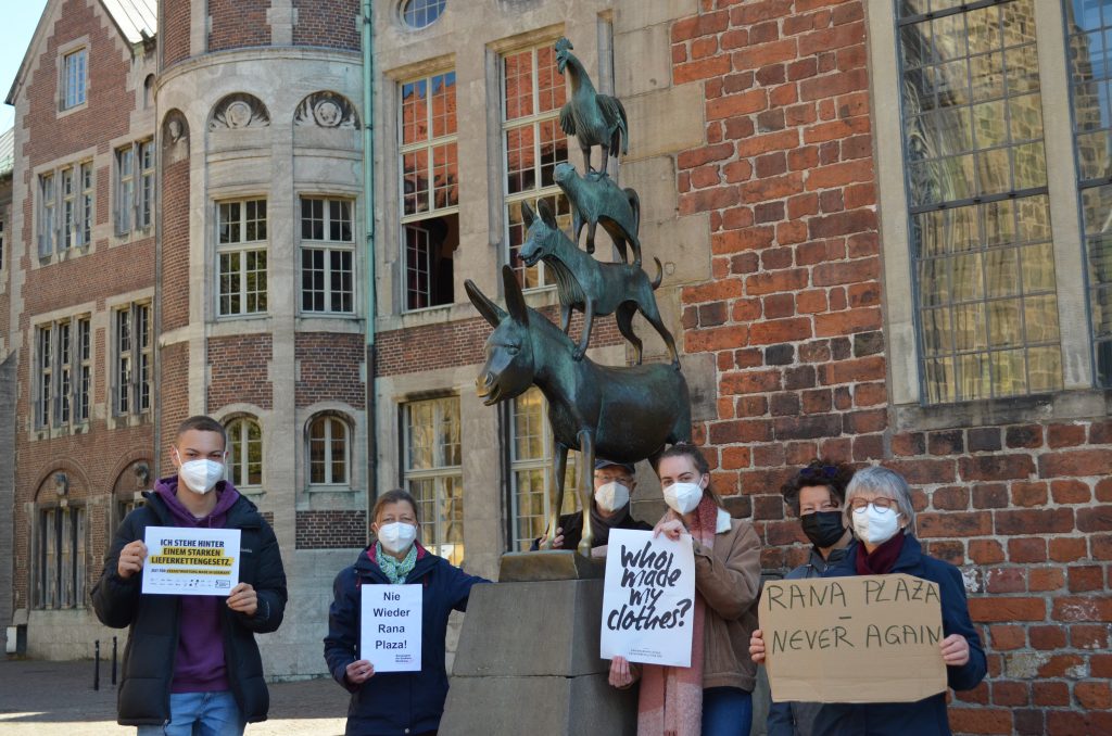 Mehrere Protestierende mit Plakaten neben der Statue der Bremer Stadtmusikanten am Rana Plaza Gedenktag