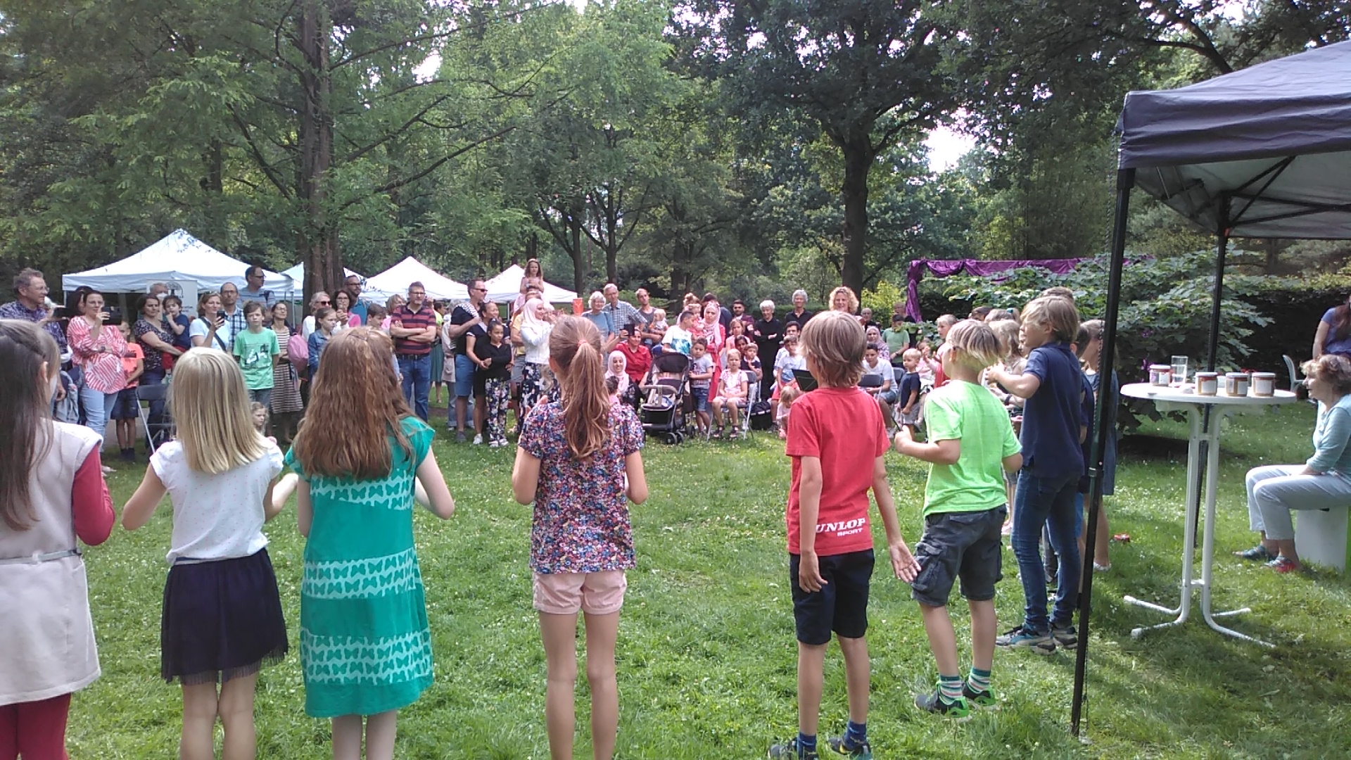 Eine Schulklasse tritt vor vielen Menschen beim KulturMitmachMarkt im Garten der Menschenrechte auf