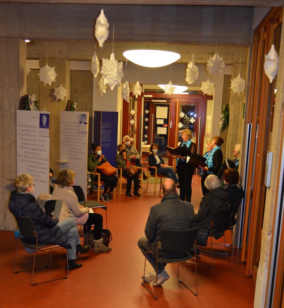 Mehrere Personen hören von der Musikgruppe Vida gesungene Lieder im Rahmen der Wanderaustellung